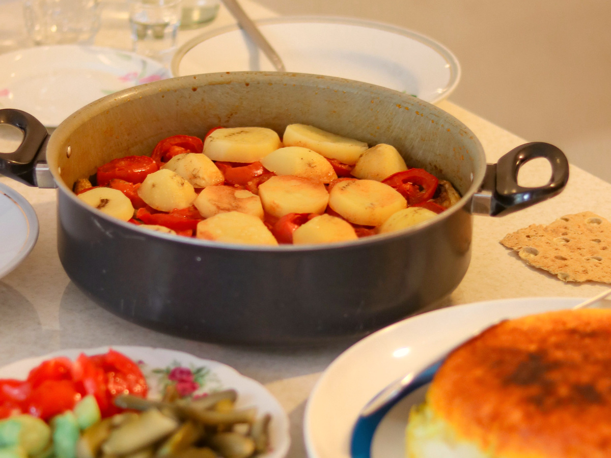 Cooked potato and tomato dish with salad, bread and rice on a dining table